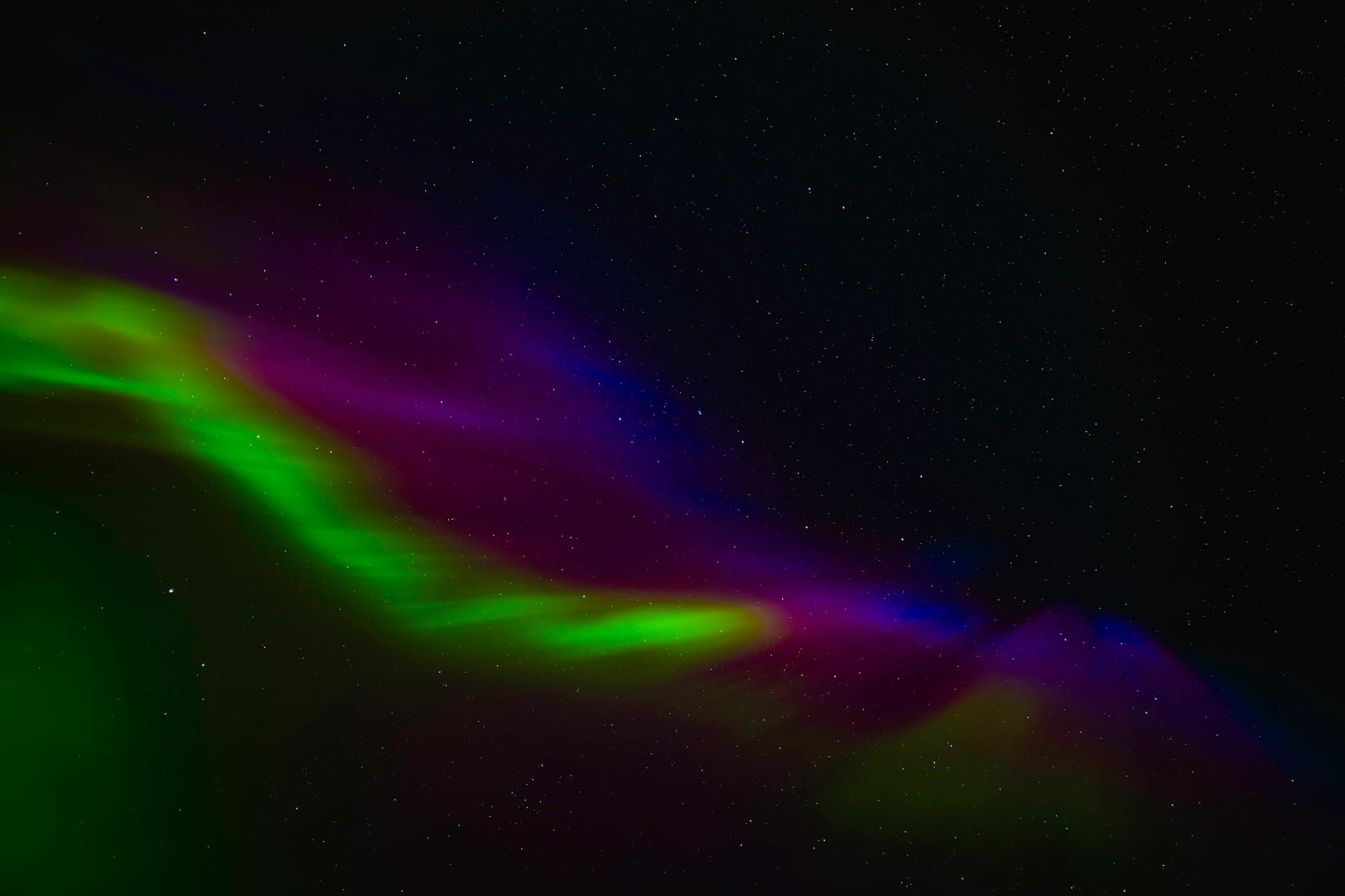 Northern lights display over dark wilderness landscape with silhouetted mountains