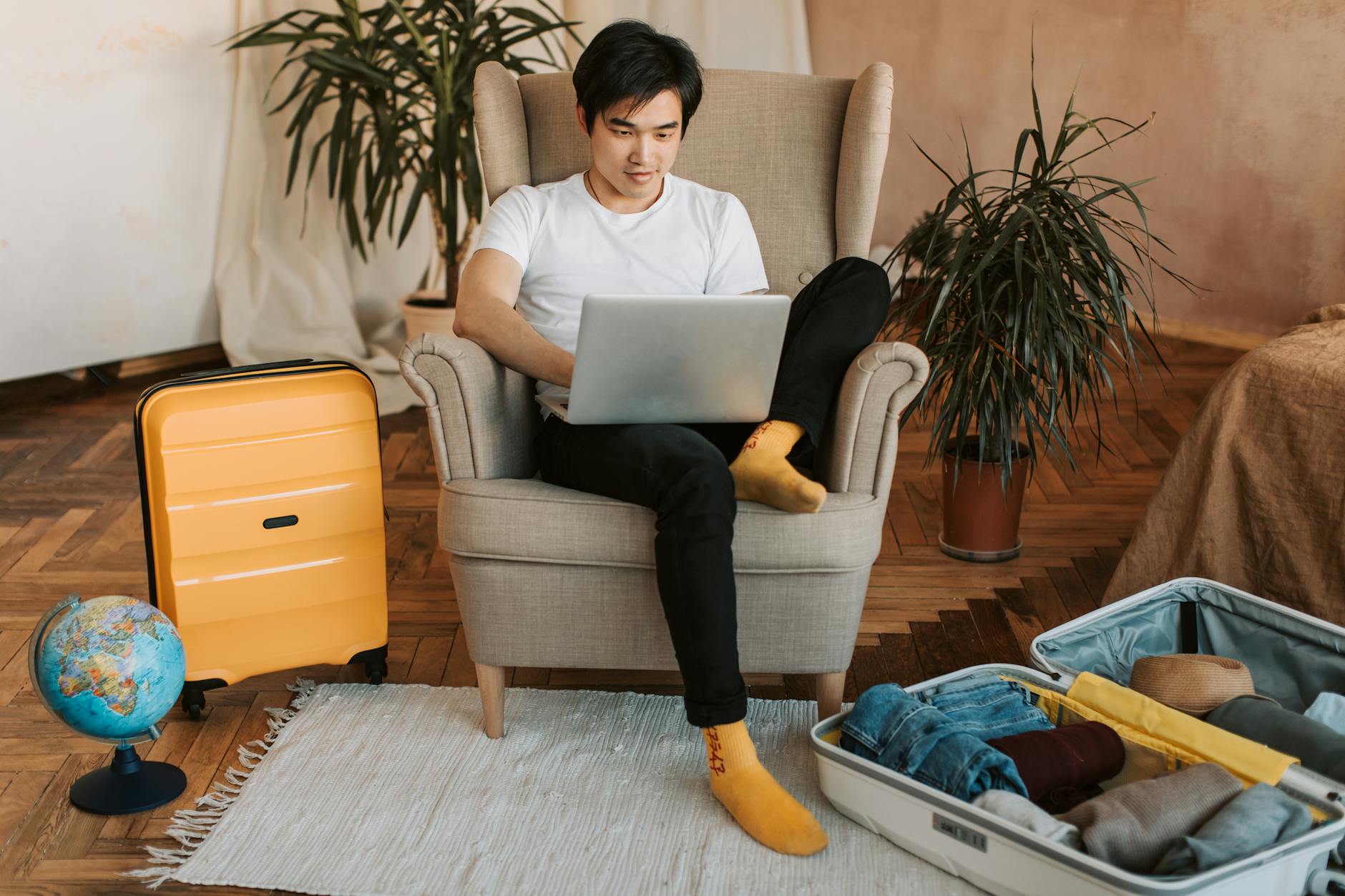 Person using laptop for travel planning with documents and coffee on desk