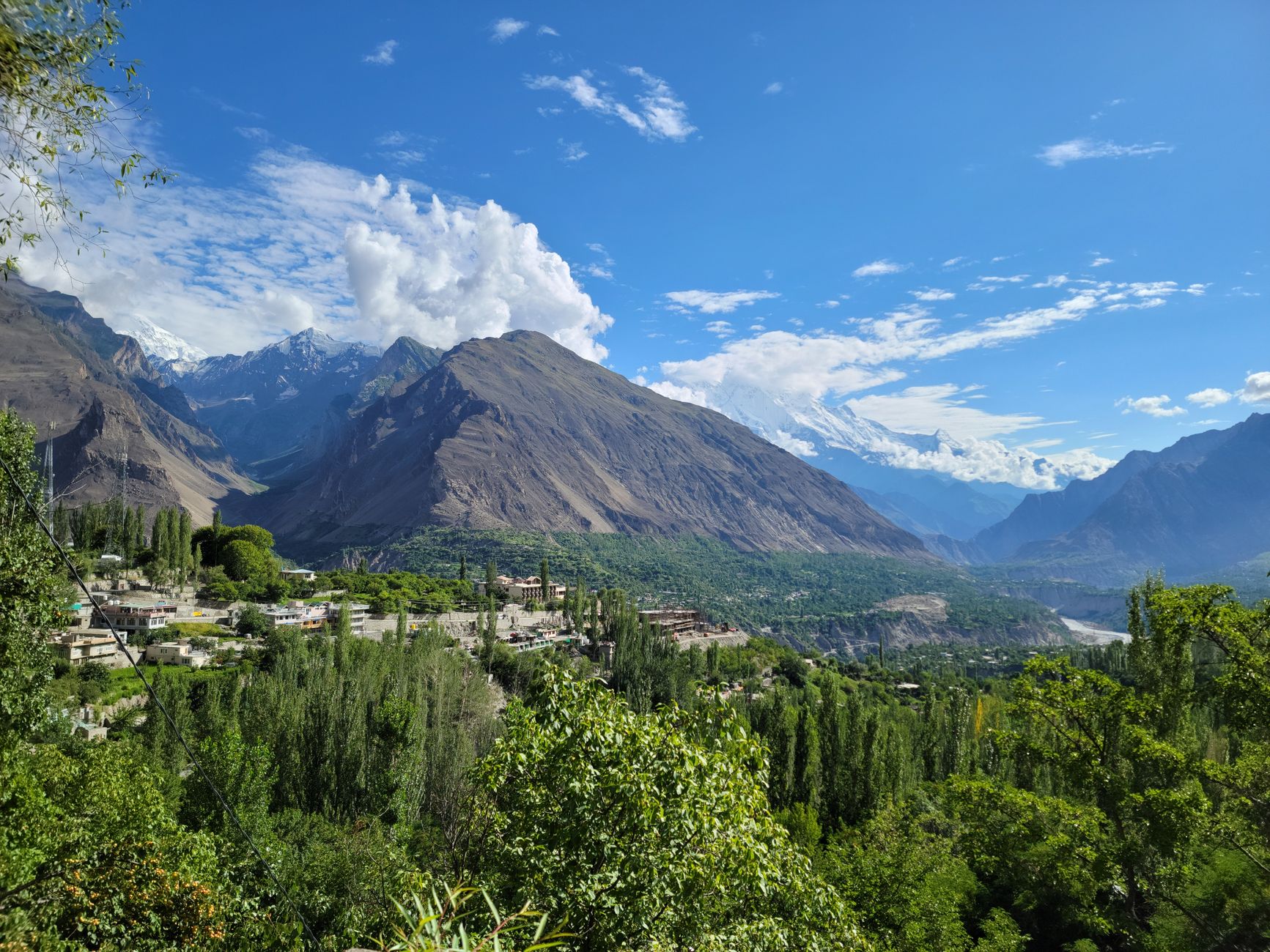 Wide view of a dramatic mountain valley in northern Pakistan with snow-capped peaks in the background