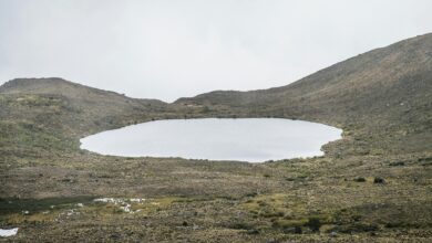 Green volcanic crater lake surrounded by Andean highlands under cloudy sky