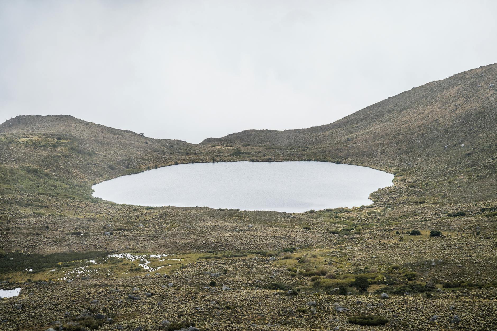 Green volcanic crater lake surrounded by Andean highlands under cloudy sky