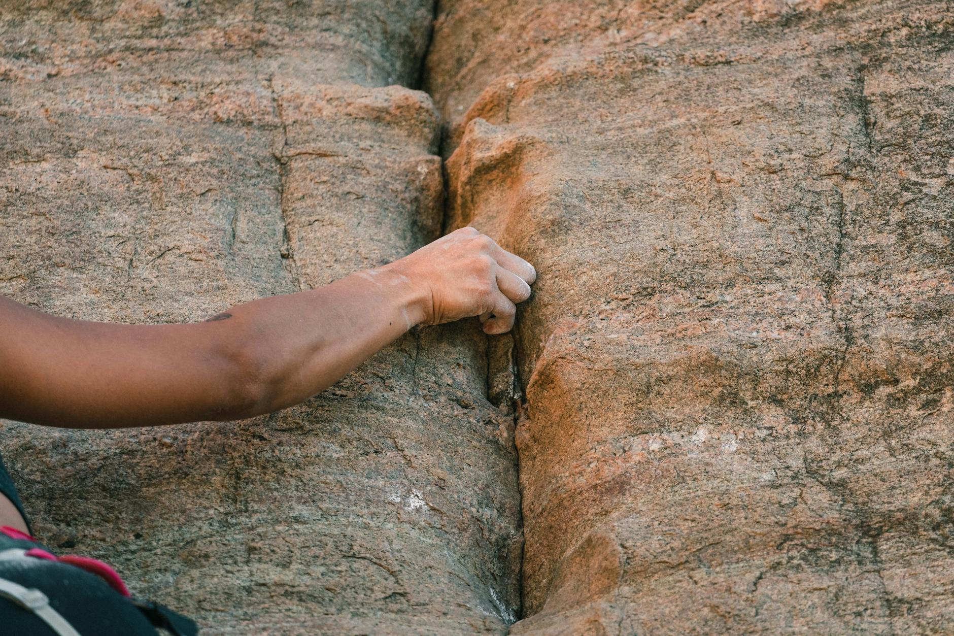 Climber ascending a bolted limestone sport route on a vertical orange-toned cliff face