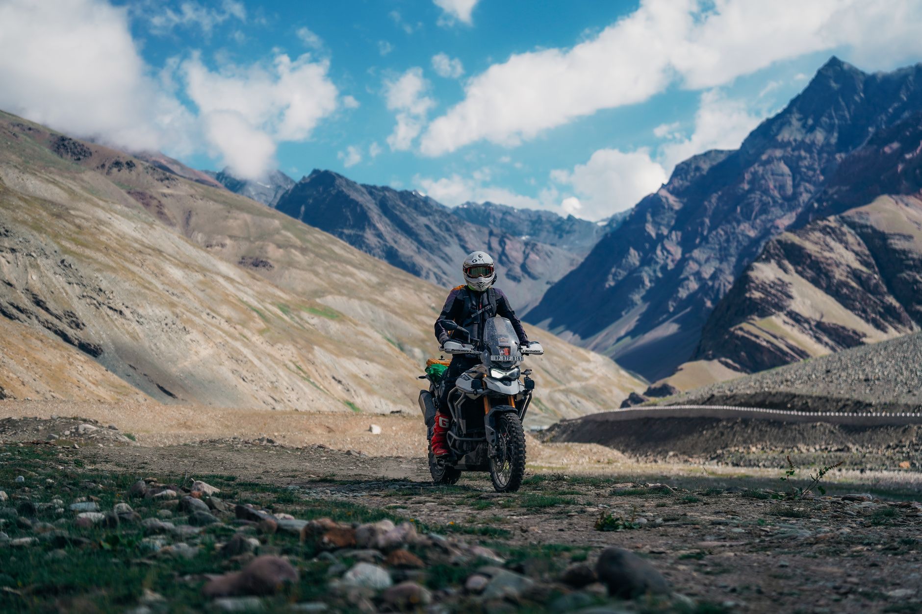A motorbike rider navigating a narrow mountain pass with steep cliffs and valley views below