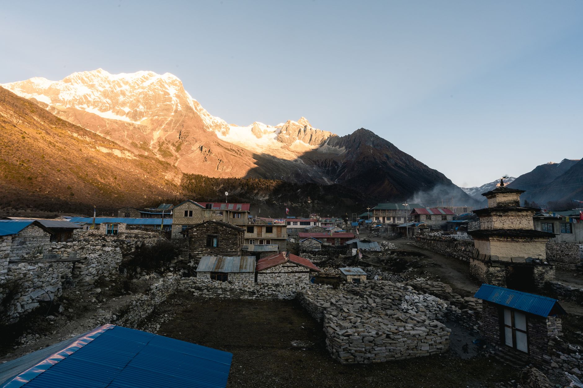 A trekker walking through a remote Nepali mountain village with traditional stone buildings