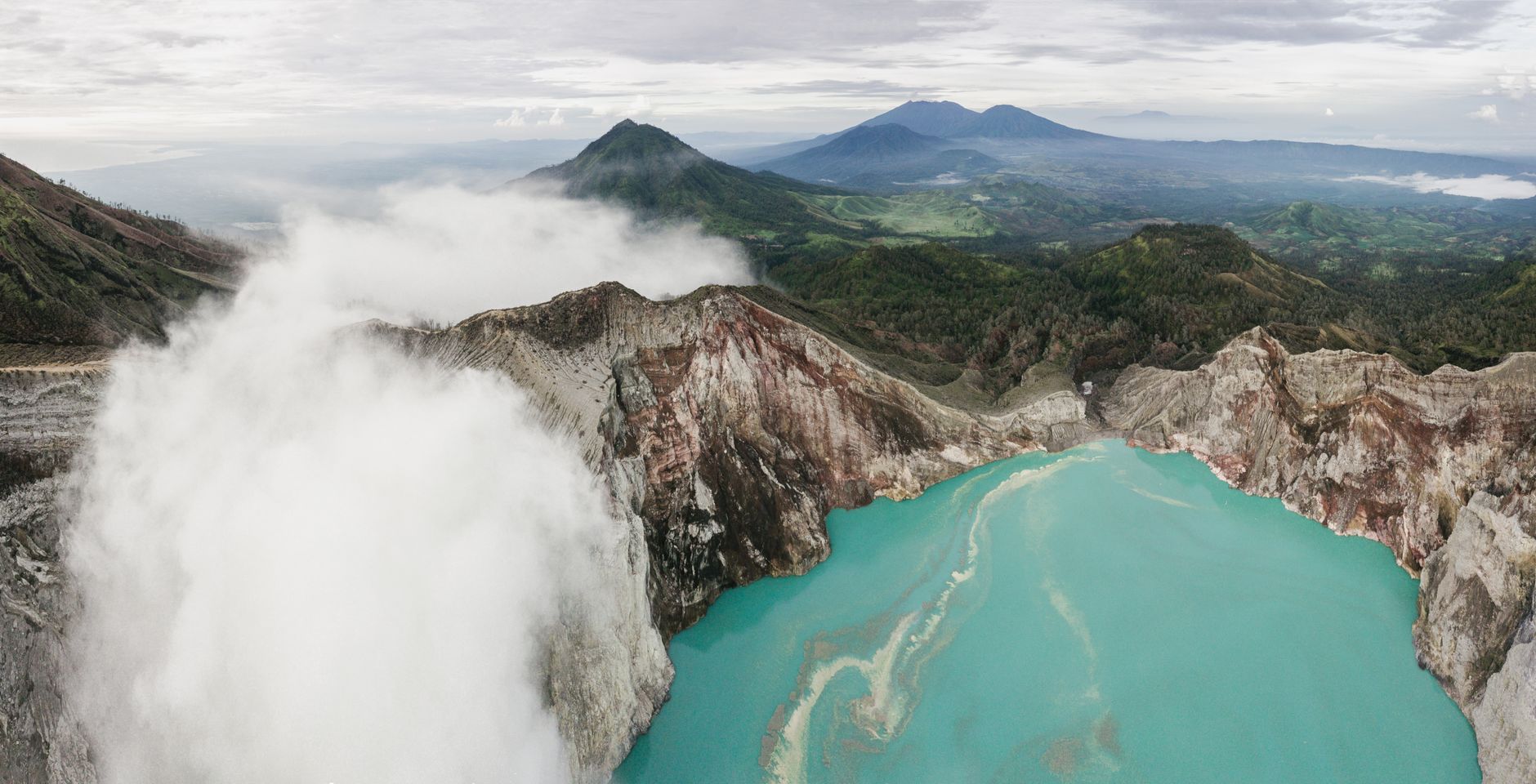 Aerial view of a turquoise volcanic crater lake surrounded by steep Andean ridgelines