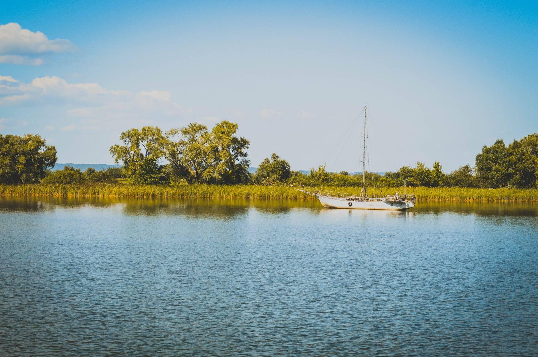 Small sailboat anchored in clear freshwater with rocky shoreline behind it