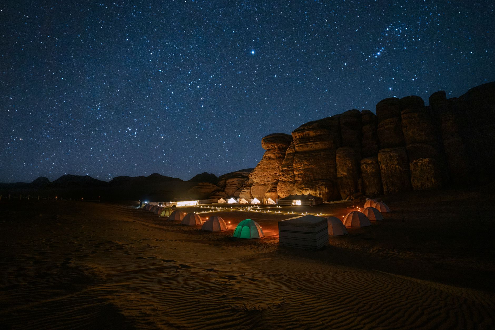 Tent campsite in an open desert with a star-filled night sky overhead