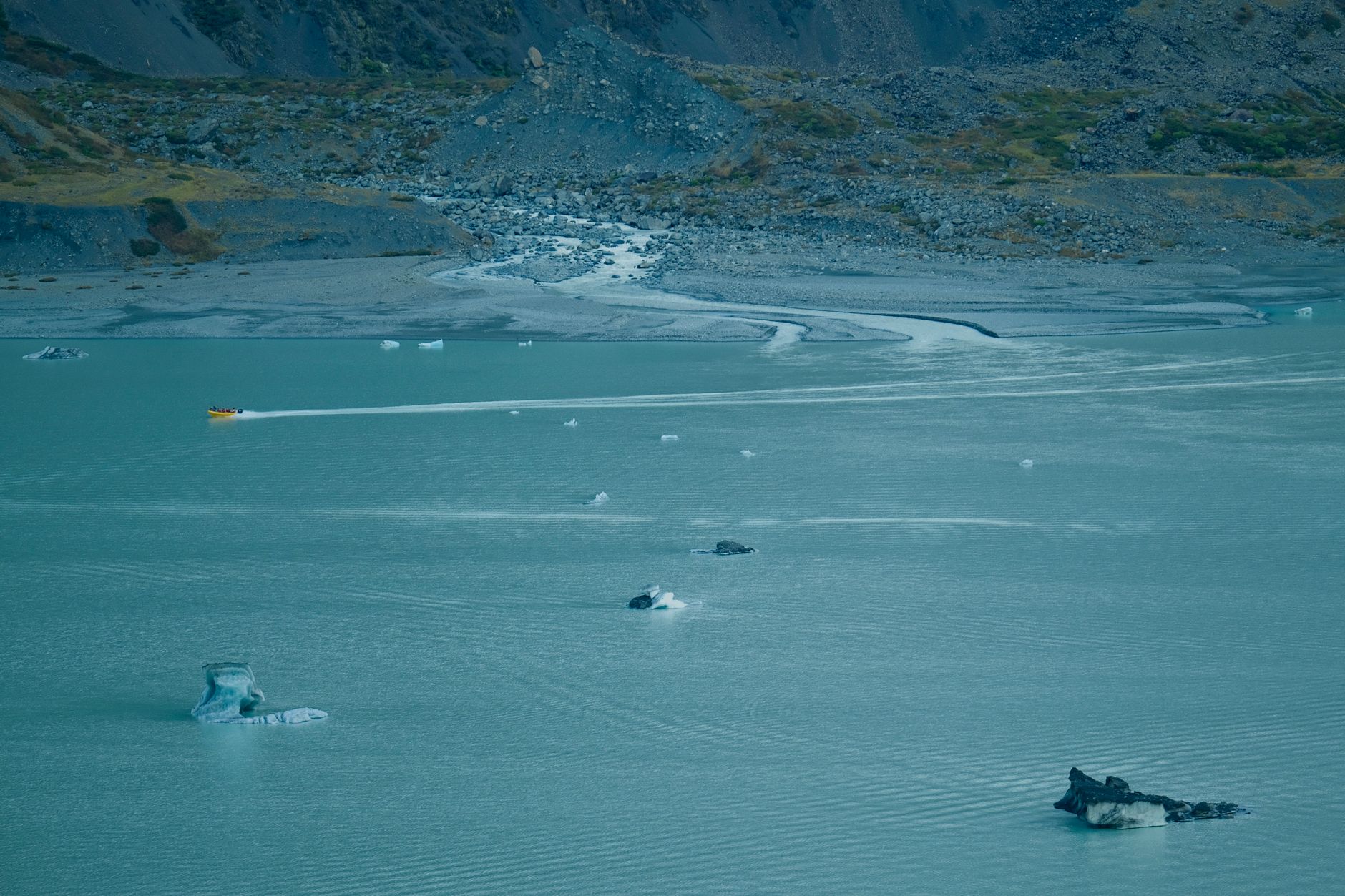Turquoise glacial lake surrounded by rocky alpine terrain and snow patches at high altitude