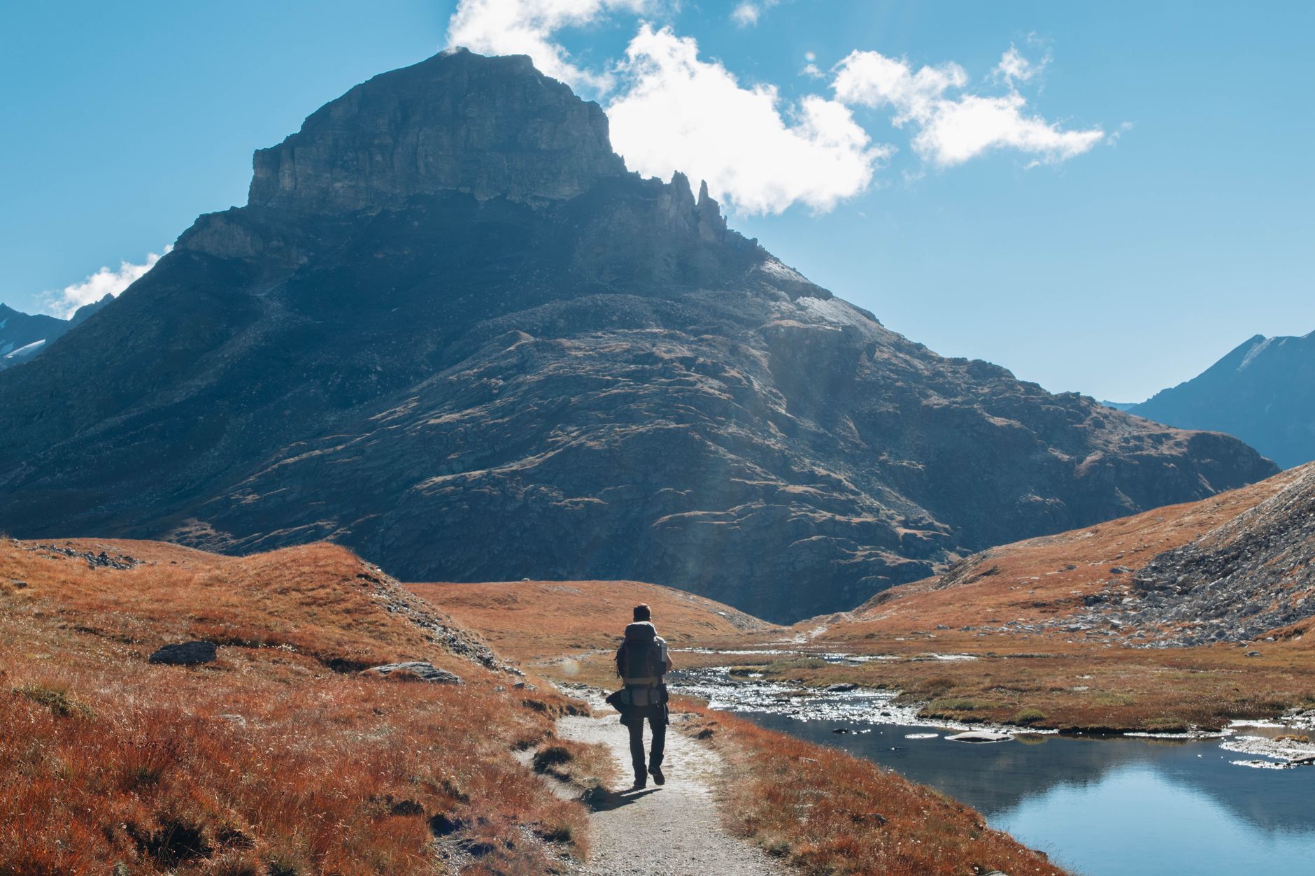 Hiker on a rocky mountain trail with dramatic ridgeline visible against a clear sky