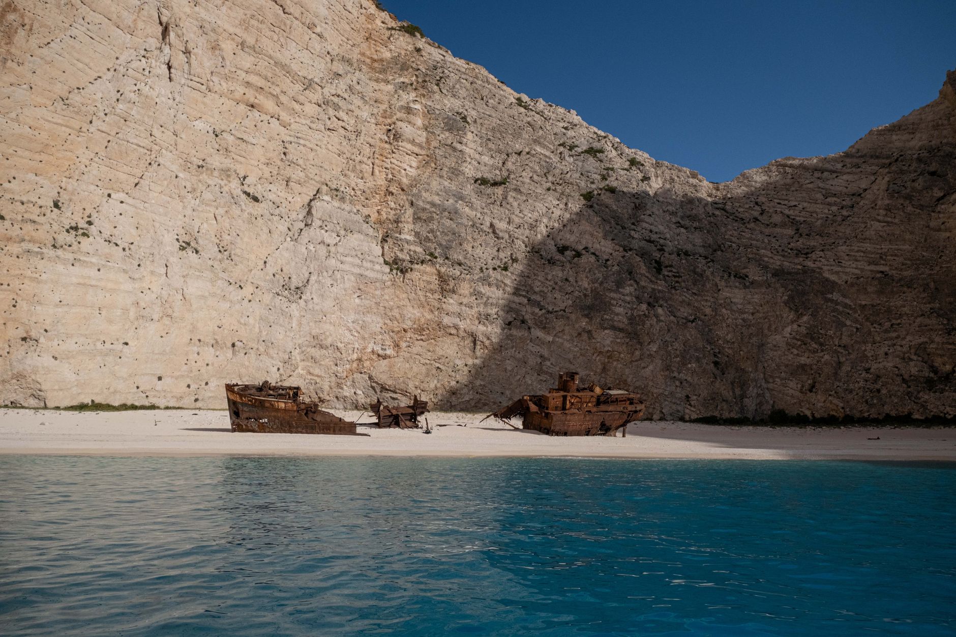 Rusted shipwreck hull resting on a remote sandy beach under grey skies