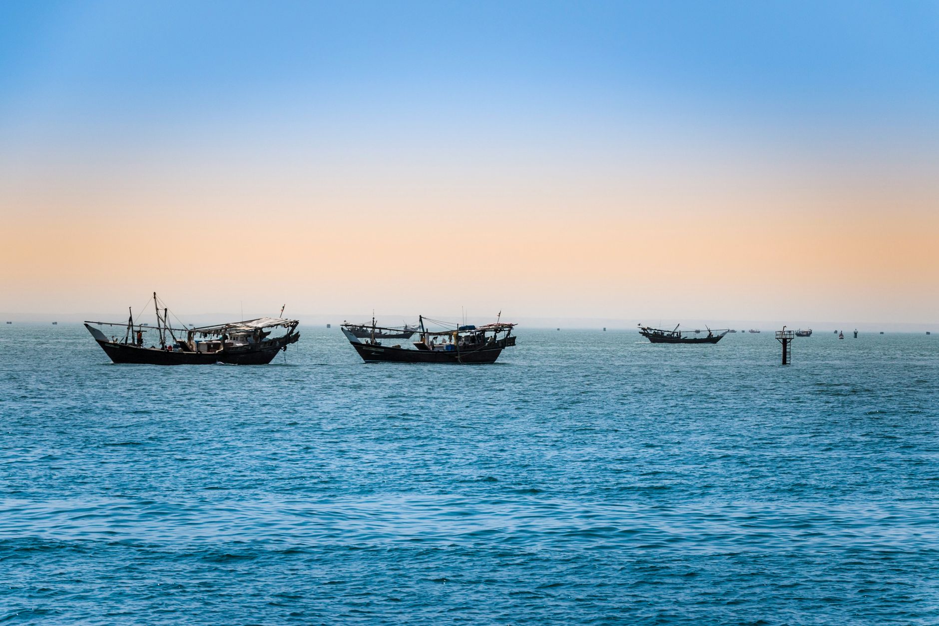 A traditional wooden dhow sailing along calm coastal waters with rocky hills visible in the background