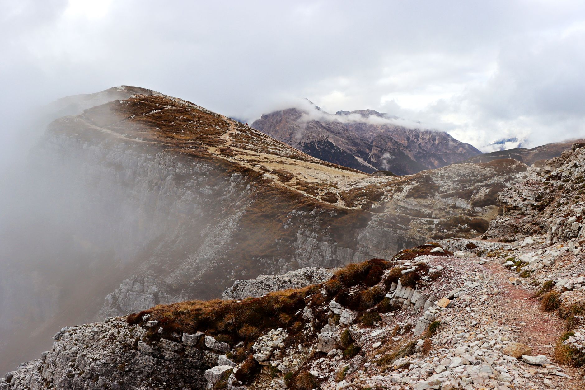 Trekker on a narrow alpine trail with low clouds rolling across rocky ridgeline