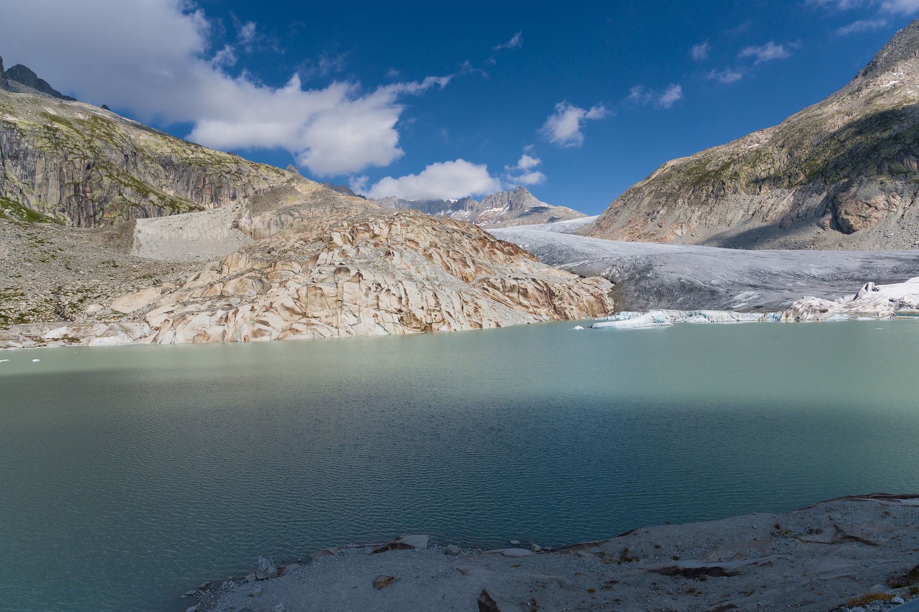 A still glacial lake surrounded by barren high-altitude terrain under a blue sky