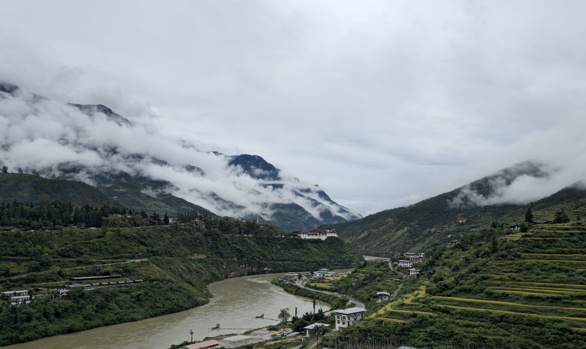 Wide green valley in Bhutan with traditional farmhouses and forested ridgelines in the background