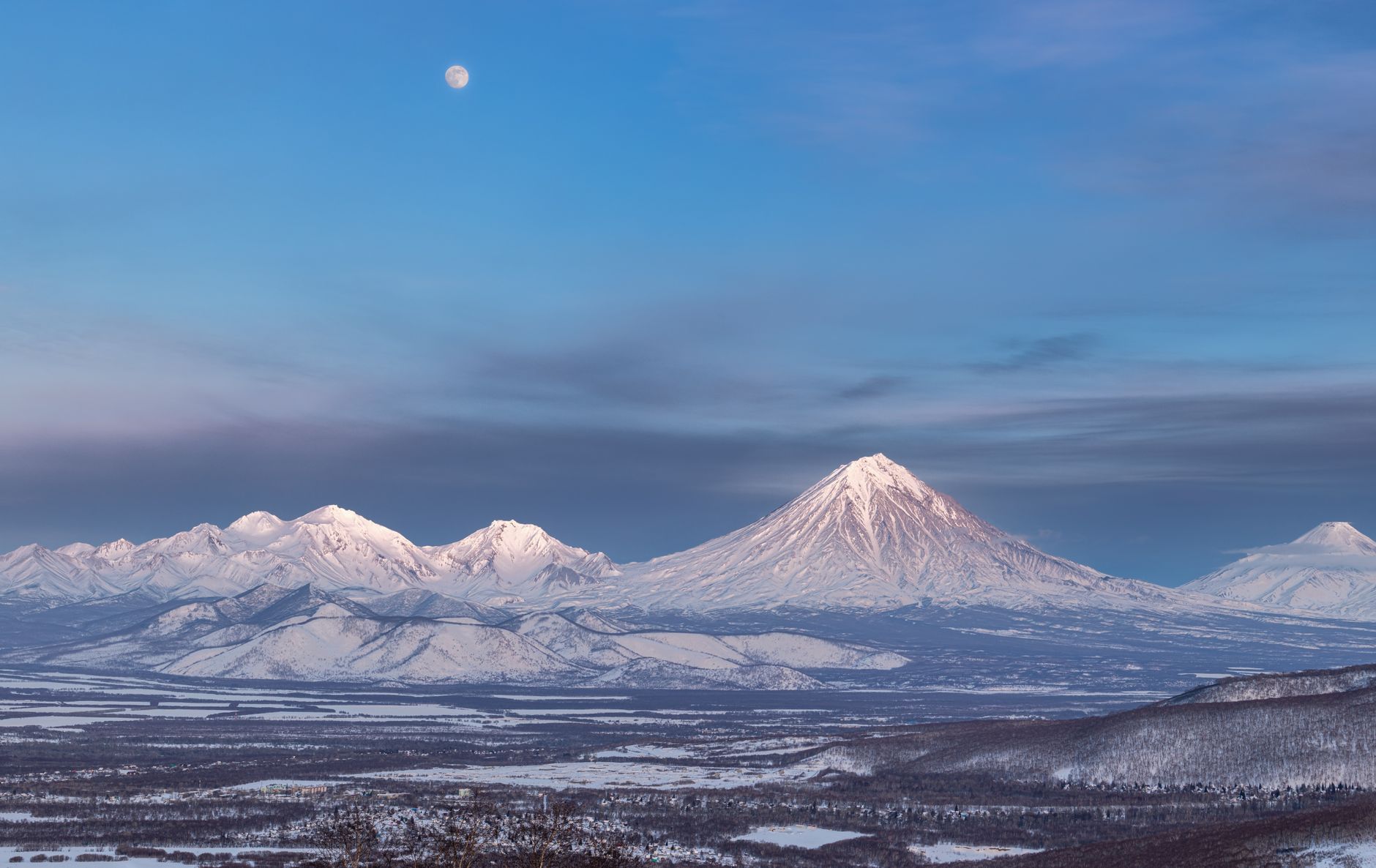 Snow-capped stratovolcano rising above an altiplano landscape at dawn