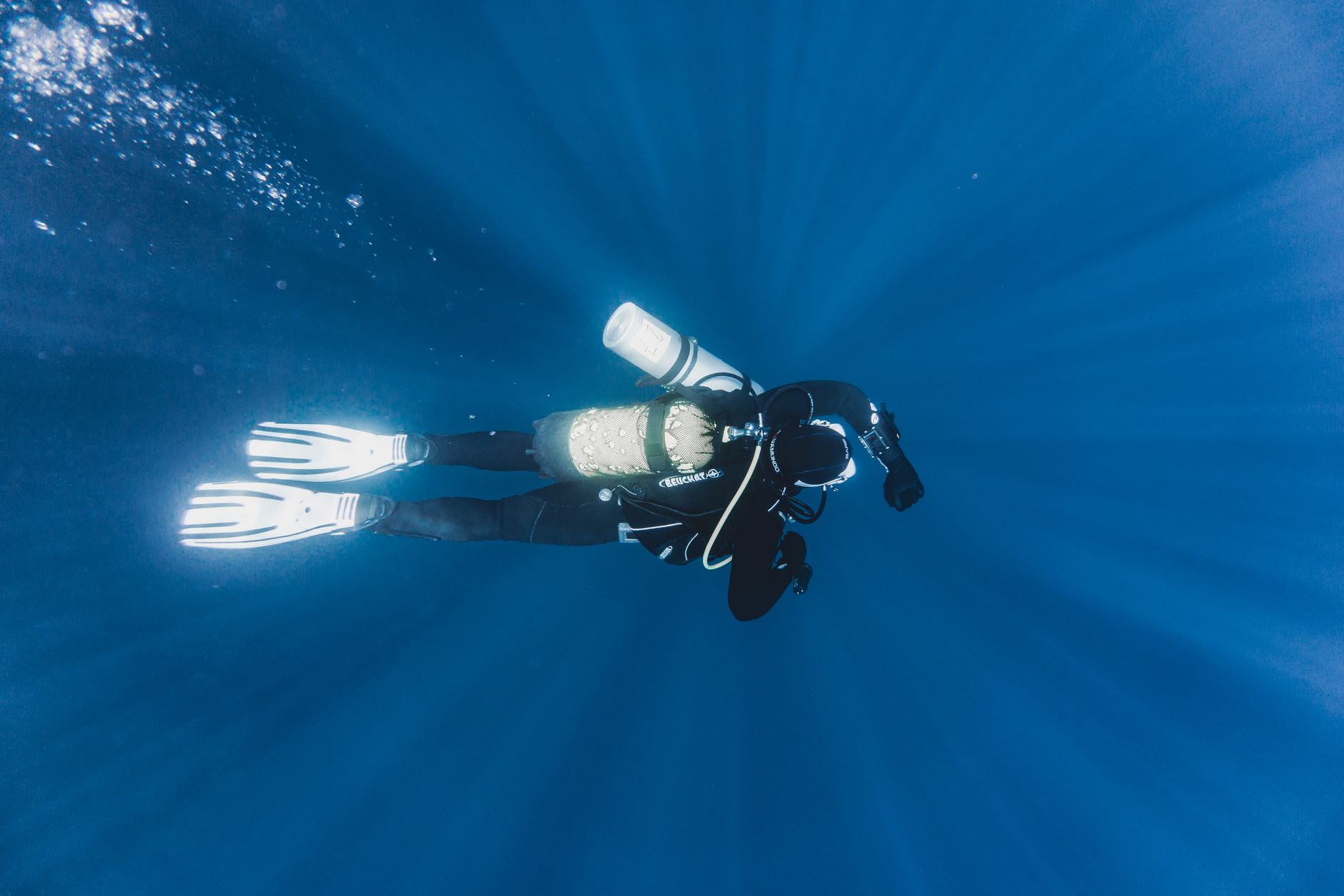 Scuba diver descending along a steep reef wall with blue water below