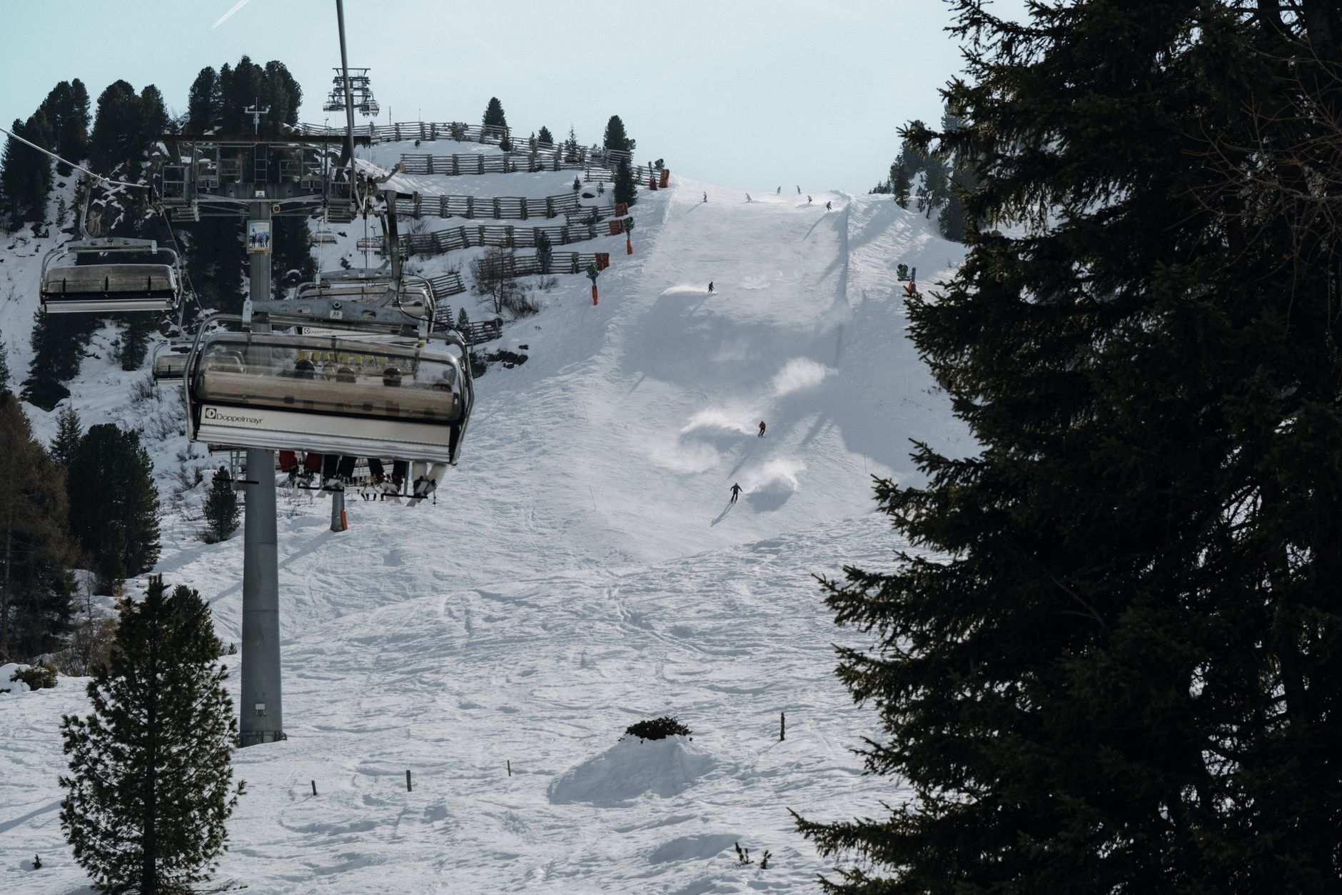 Skier descending a steep powder slope through sparse mountain trees in winter conditions