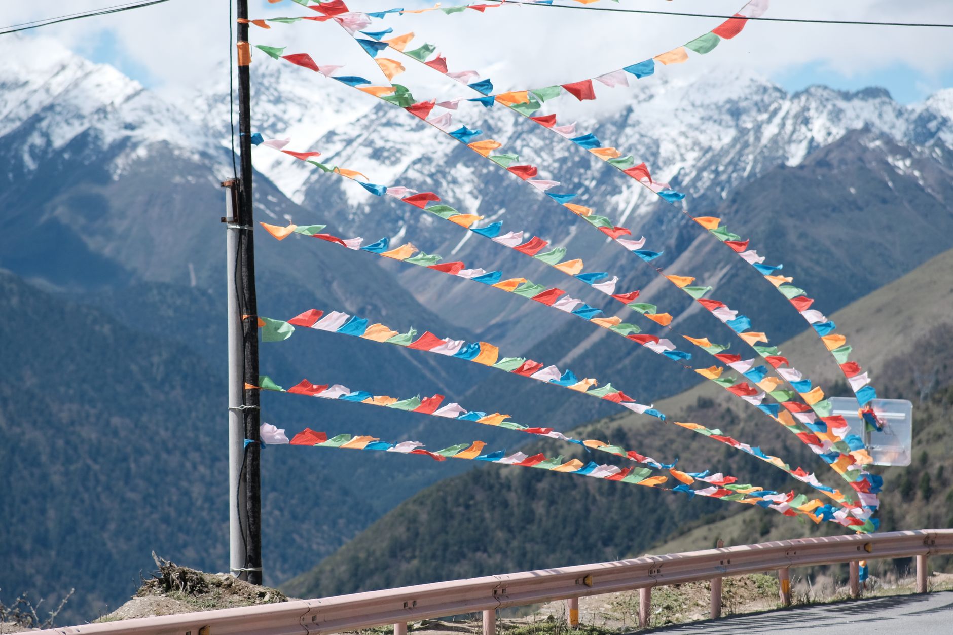 Colorful Buddhist prayer flags stretching across a high mountain pass with snow peaks visible beyond